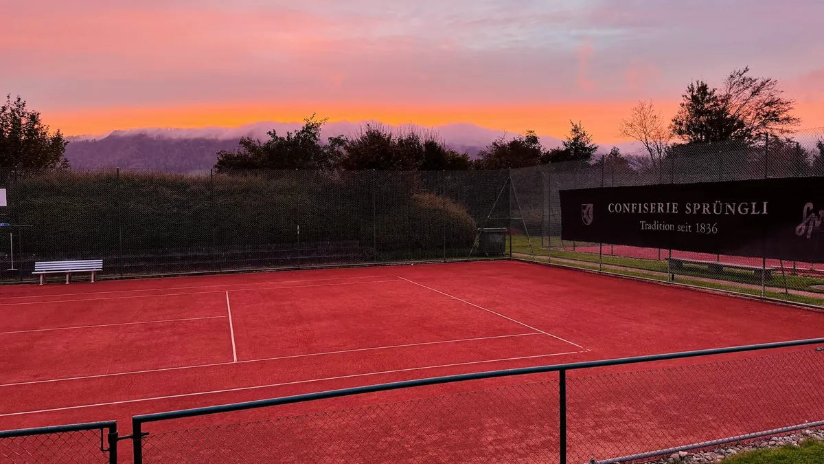 Ein leerer Allwetterplatz im letzten Abendlicht, der Himmel darüber orange und violett